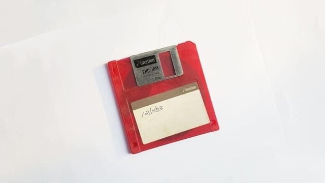 Ancienne disquette d’ordinateur datant de 2003, rouge posée sur un fond blanc.