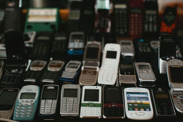 Une multitude de vieux téléphones à clapets sont ouverts sur une table pour montrer les déchets électroniques provoqués par l’obsolescence psychologique